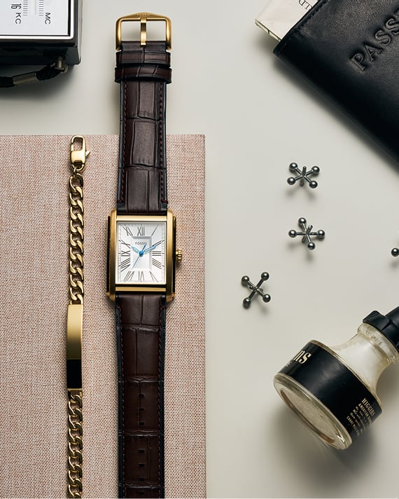 Top-down shot of a desk with a Fossil men's ID bracelet and gold-tone Fossil Carraway watch with a brown leather croco-style strap
