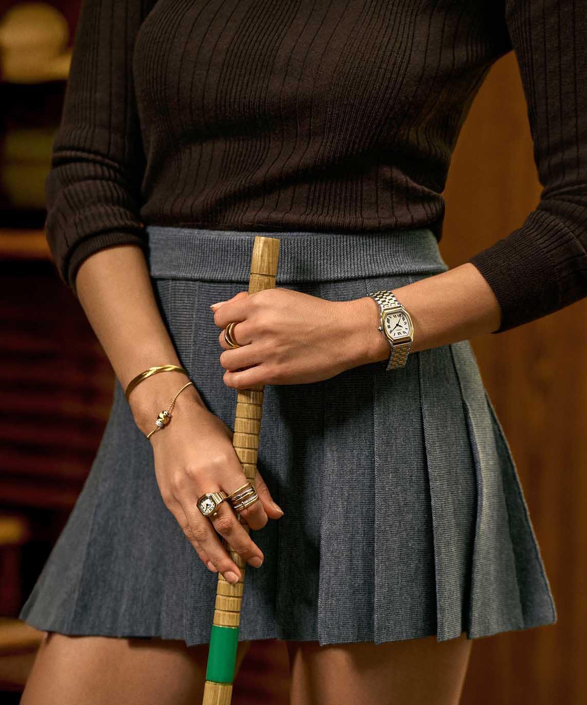 A tight crop of a woman's waist featuring her hands and arms decorated with multiple Fossil watches and jewellery.